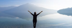 Woman with open arms by the lake on a background of mountains. Enjoying optimal health