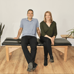 Dr Laina & Dr Jamie sitting on Chiropractic table smiling in London Ontario